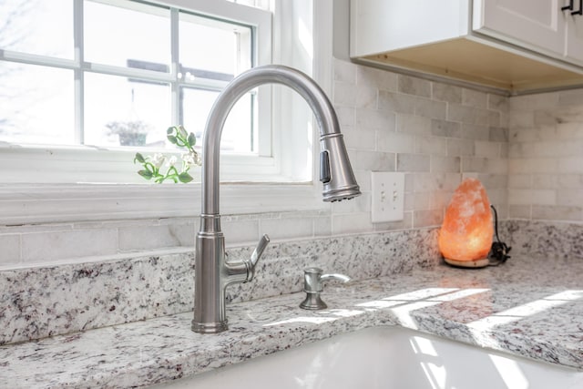 interior details with light stone counters, a sink, white cabinetry, and decorative backsplash