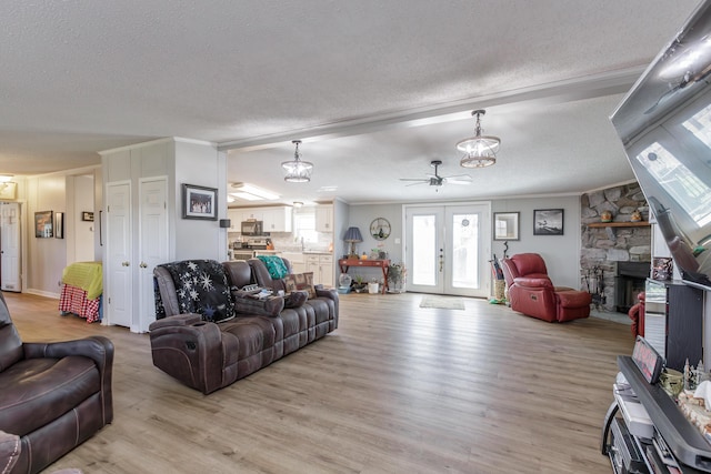 living room with ornamental molding, a textured ceiling, french doors, light wood-type flooring, and a fireplace