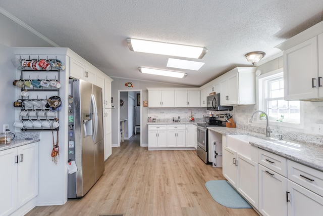 kitchen featuring light wood-style flooring, stainless steel appliances, white cabinets, vaulted ceiling, and tasteful backsplash