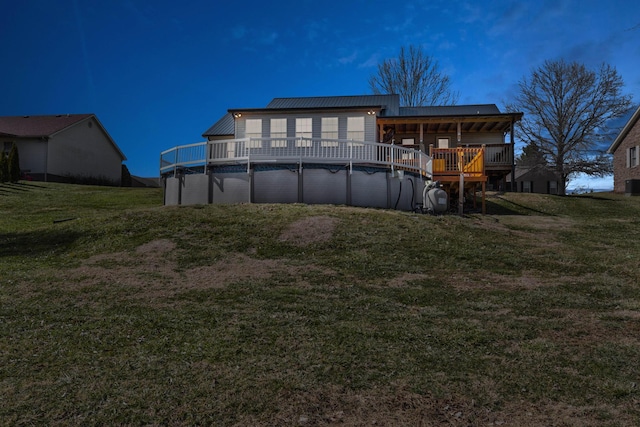 rear view of house with metal roof, a yard, a deck, and a covered pool