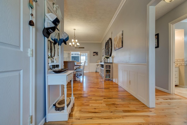 interior space with wainscoting, a textured ceiling, crown molding, light wood-style floors, and a chandelier