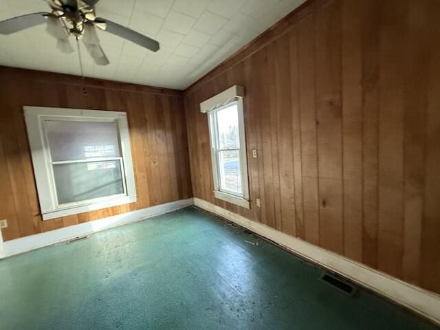 empty room featuring wood walls, baseboards, visible vents, and ceiling fan