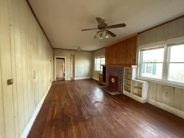 unfurnished living room featuring dark wood-style flooring, ornamental molding, ceiling fan, a tile fireplace, and baseboards