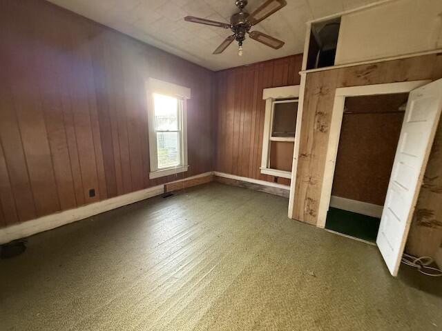 interior space with a ceiling fan, wood walls, and baseboards