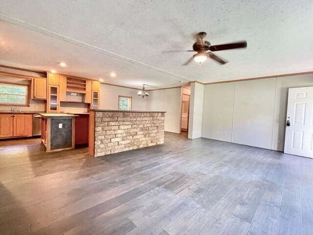 unfurnished living room featuring a textured ceiling, ornamental molding, ceiling fan with notable chandelier, and wood finished floors