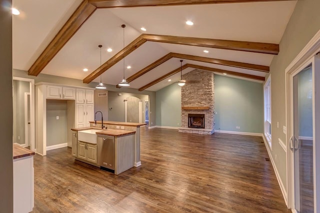 kitchen featuring a sink, vaulted ceiling with beams, dark wood-type flooring, a fireplace, and stainless steel dishwasher