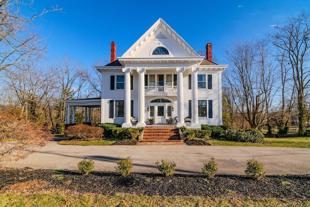 greek revival inspired property featuring covered porch, a chimney, and a balcony