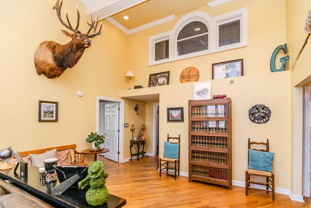 sitting room with baseboards, a high ceiling, wood finished floors, and crown molding