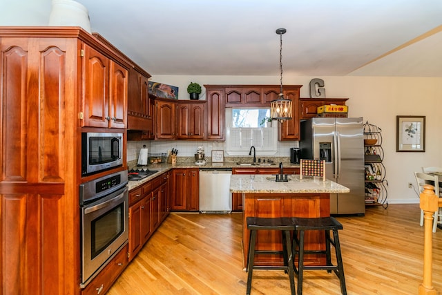 kitchen with appliances with stainless steel finishes, backsplash, light wood-style flooring, and a kitchen breakfast bar