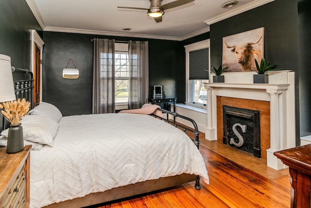 bedroom with crown molding, multiple windows, a fireplace, and wood finished floors