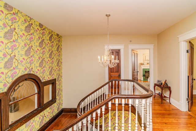 stairway with baseboards, a fireplace, wood finished floors, and wallpapered walls