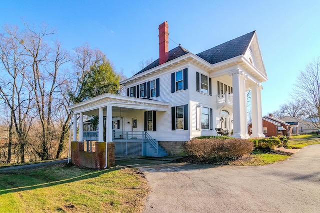 greek revival inspired property featuring covered porch, a chimney, and a front yard