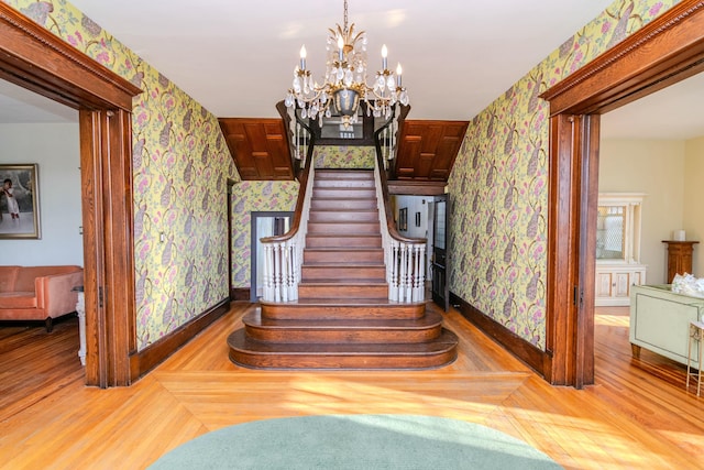 stairs featuring wallpapered walls, baseboards, a chandelier, and wood finished floors