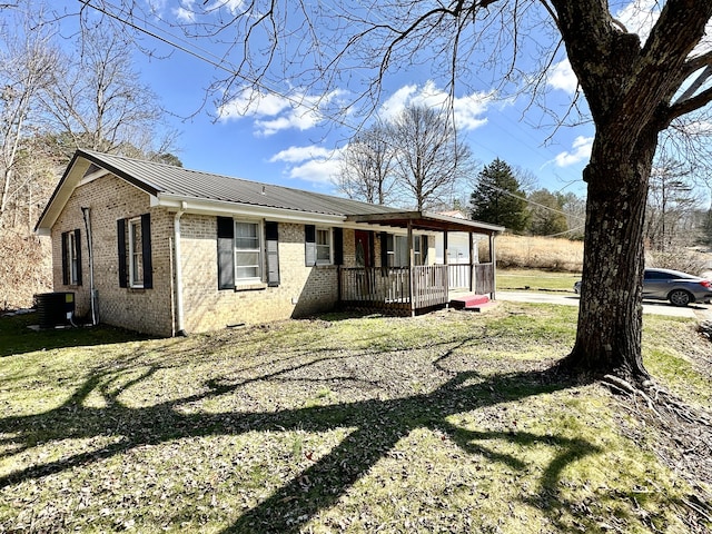 view of front facade featuring metal roof, brick siding, a front yard, and cooling unit