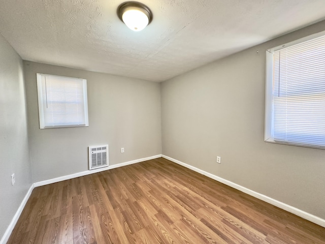 unfurnished room featuring heating unit, a healthy amount of sunlight, wood finished floors, and baseboards