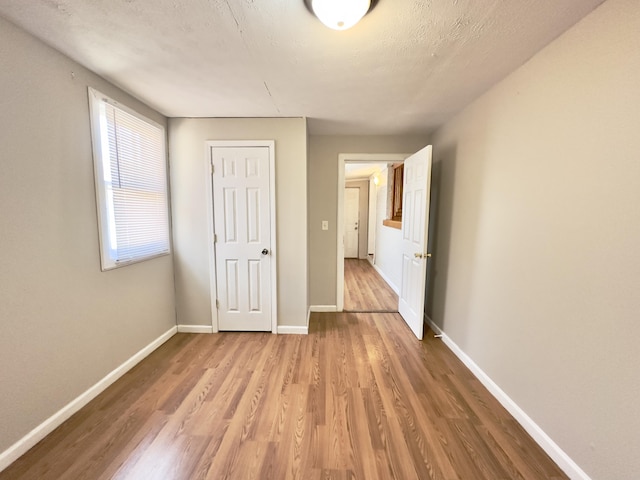 unfurnished bedroom with a textured ceiling, light wood-type flooring, and baseboards