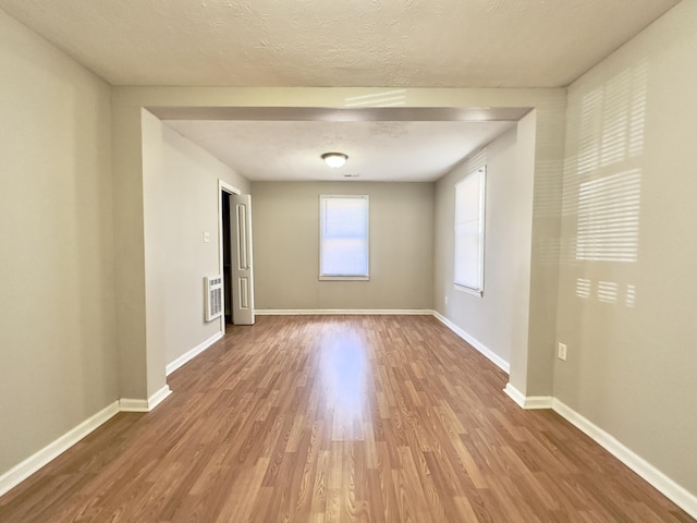 empty room with heating unit, a textured ceiling, baseboards, and wood finished floors