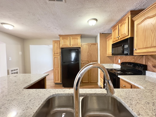 kitchen with light wood-style flooring, a sink, a textured ceiling, light stone countertops, and black appliances