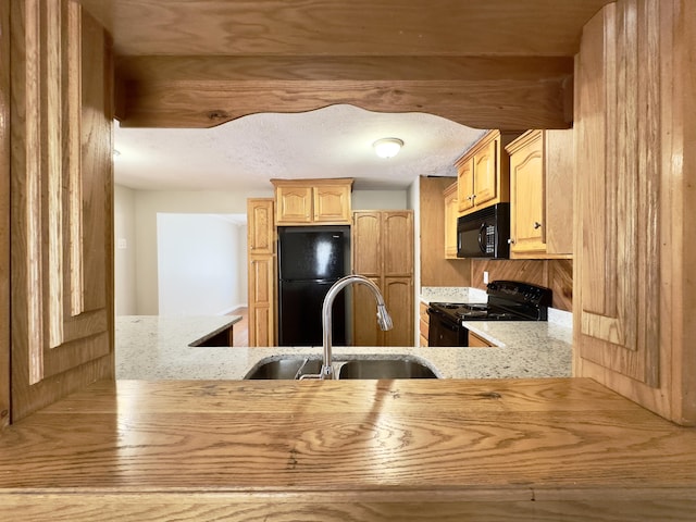 kitchen with light stone countertops, a textured ceiling, light brown cabinetry, black appliances, and a sink