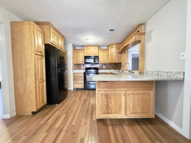 kitchen with a peninsula, a sink, visible vents, black appliances, and wood-type flooring