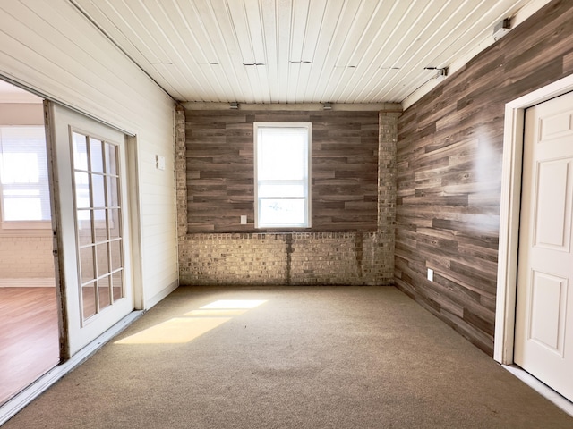 empty room featuring carpet floors, wood walls, brick wall, and wooden ceiling