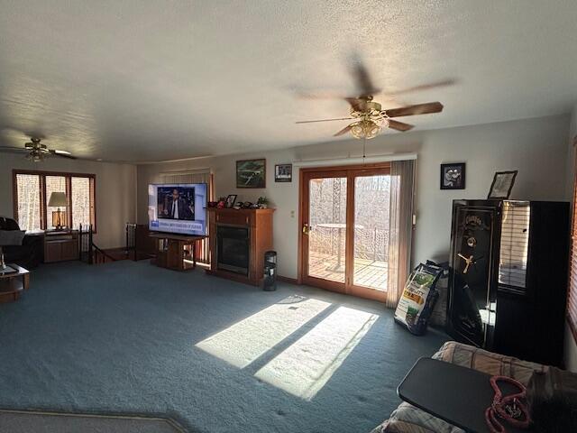 carpeted living area featuring ceiling fan, a fireplace, and a textured ceiling