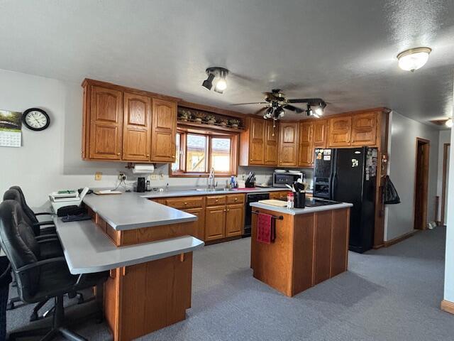 kitchen with a peninsula, black appliances, a breakfast bar, and brown cabinets