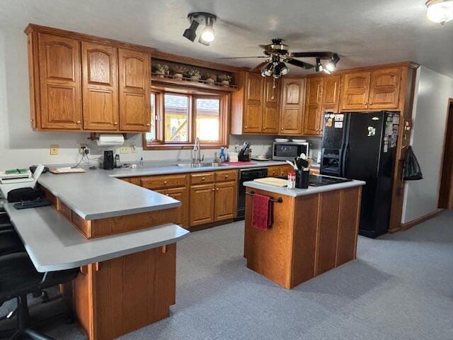 kitchen featuring black appliances, a peninsula, a sink, and brown cabinets