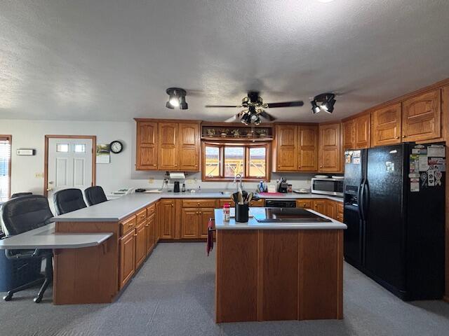 kitchen with black appliances, a peninsula, light countertops, and brown cabinets