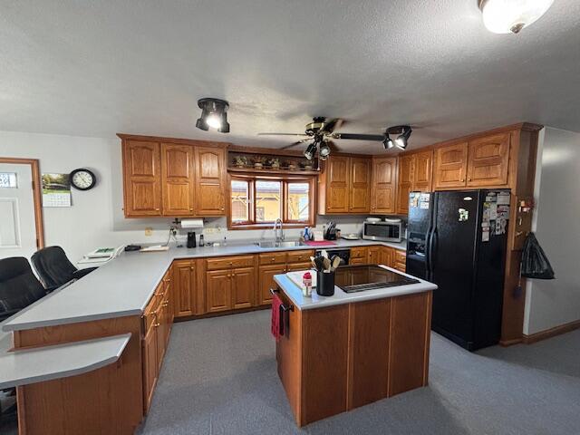 kitchen with a peninsula, a sink, black fridge, brown cabinets, and stainless steel microwave