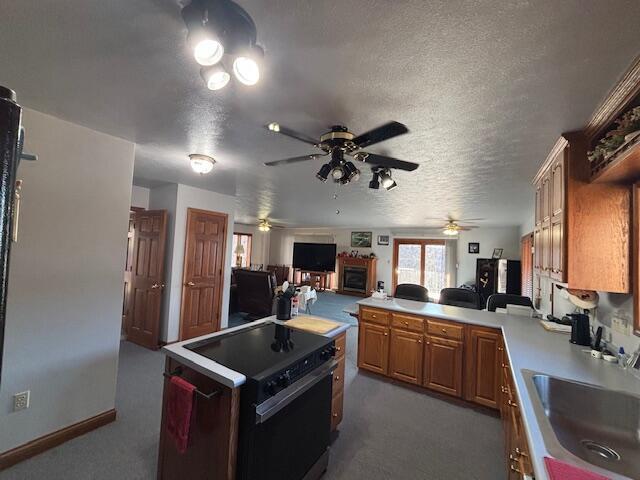 kitchen featuring range with electric stovetop, a sink, open floor plan, light countertops, and dark colored carpet