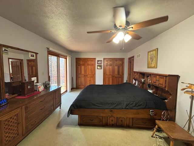 carpeted bedroom with access to exterior, two closets, visible vents, a ceiling fan, and a textured ceiling