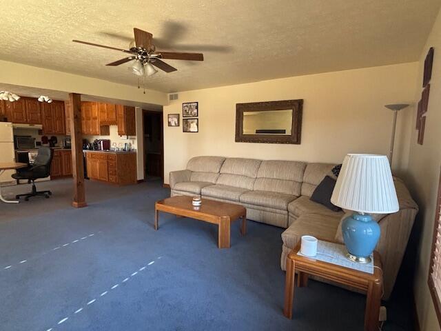 carpeted living room with a ceiling fan and a textured ceiling