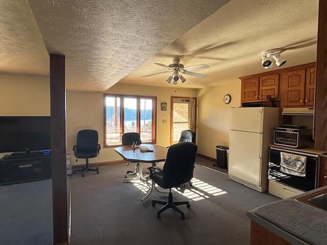 home office featuring a textured ceiling, dark colored carpet, a ceiling fan, and baseboards