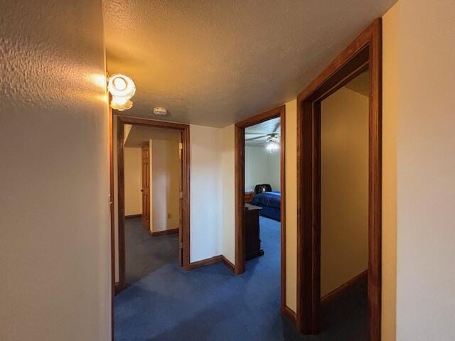 hallway with baseboards, dark colored carpet, and a textured ceiling