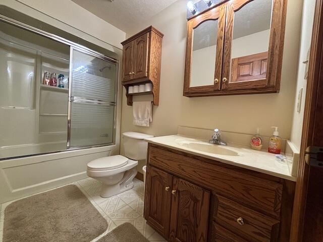 full bath featuring bath / shower combo with glass door, tile patterned flooring, vanity, and toilet