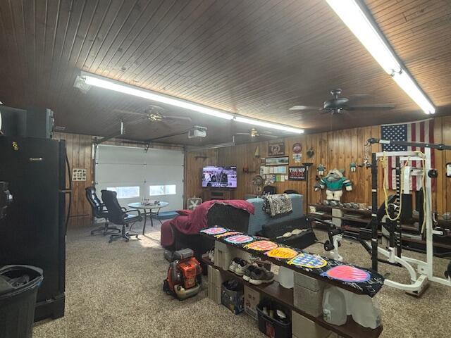 garage with a garage door opener, freestanding refrigerator, wooden walls, and a ceiling fan