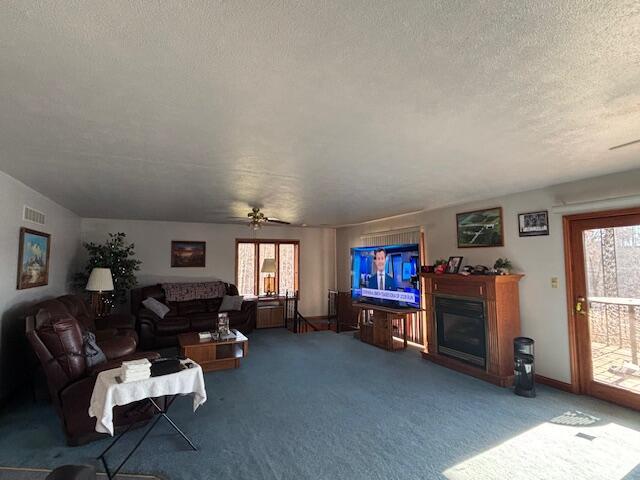 carpeted living area with ceiling fan, visible vents, a textured ceiling, and a glass covered fireplace