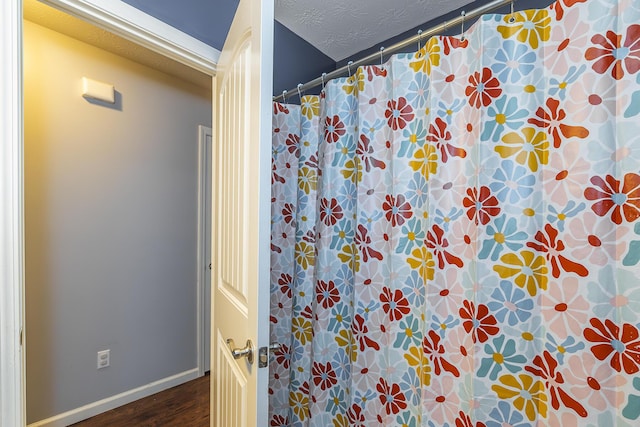 full bathroom featuring a shower with shower curtain, baseboards, a textured ceiling, and wood finished floors