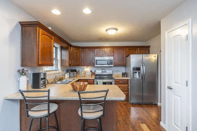 kitchen with dark wood finished floors, appliances with stainless steel finishes, a peninsula, light countertops, and a sink