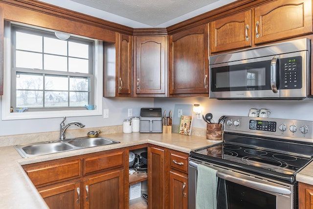 kitchen with light countertops, appliances with stainless steel finishes, brown cabinetry, a sink, and a textured ceiling