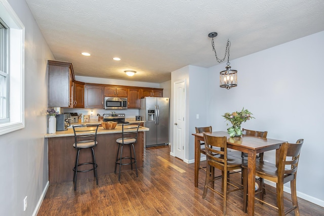 kitchen with a textured ceiling, a peninsula, dark wood-style flooring, baseboards, and appliances with stainless steel finishes