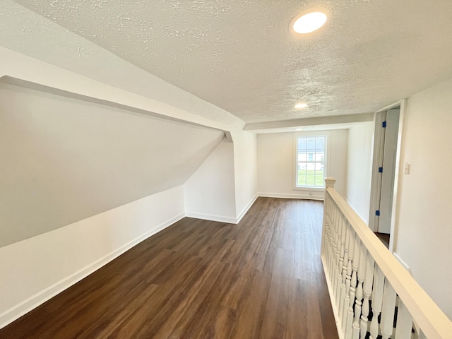 bonus room with lofted ceiling, a textured ceiling, dark wood-type flooring, and baseboards