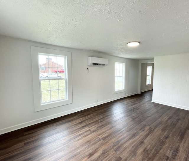 empty room with dark wood-style floors, a textured ceiling, baseboards, and a wall unit AC