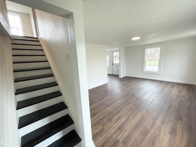 stairs with wood finished floors, baseboards, and a textured ceiling