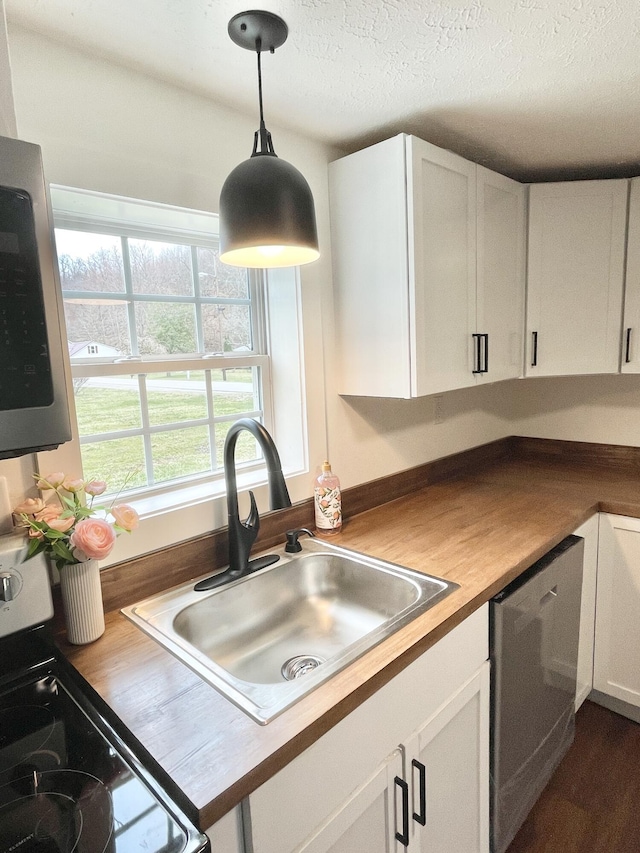 kitchen featuring butcher block countertops, hanging light fixtures, white cabinets, stainless steel appliances, and a sink