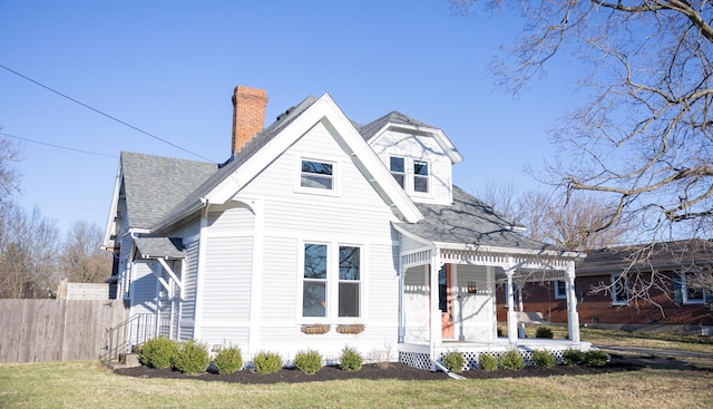 view of front of house featuring a front lawn, roof with shingles, a chimney, and fence