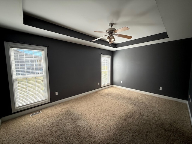 carpeted spare room with ceiling fan, a tray ceiling, visible vents, and baseboards