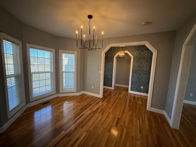 unfurnished dining area with arched walkways, wood finished floors, visible vents, and baseboards