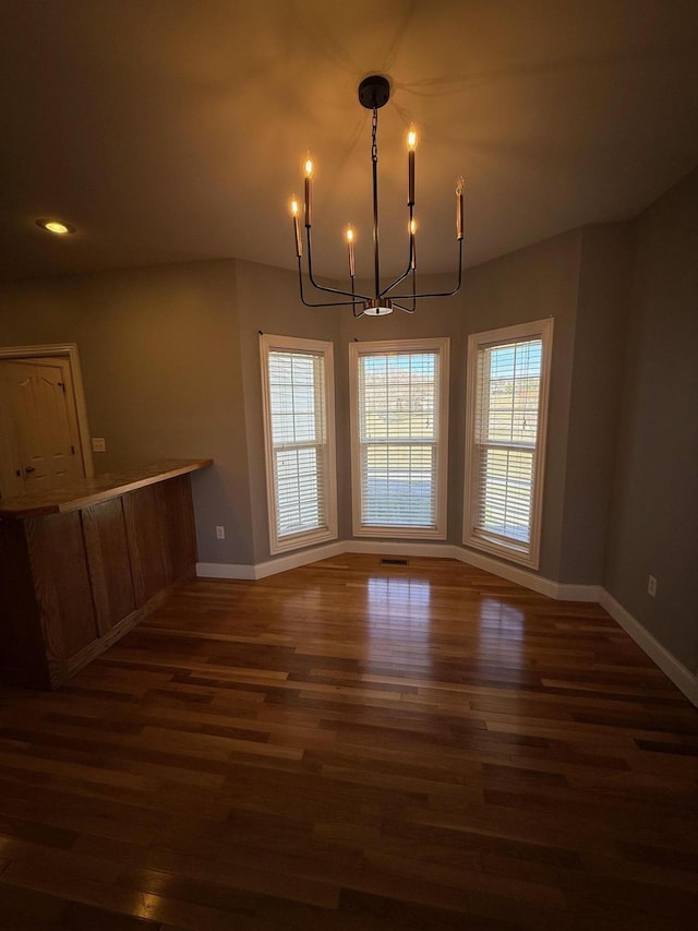 unfurnished dining area with a chandelier, wood finished floors, and baseboards